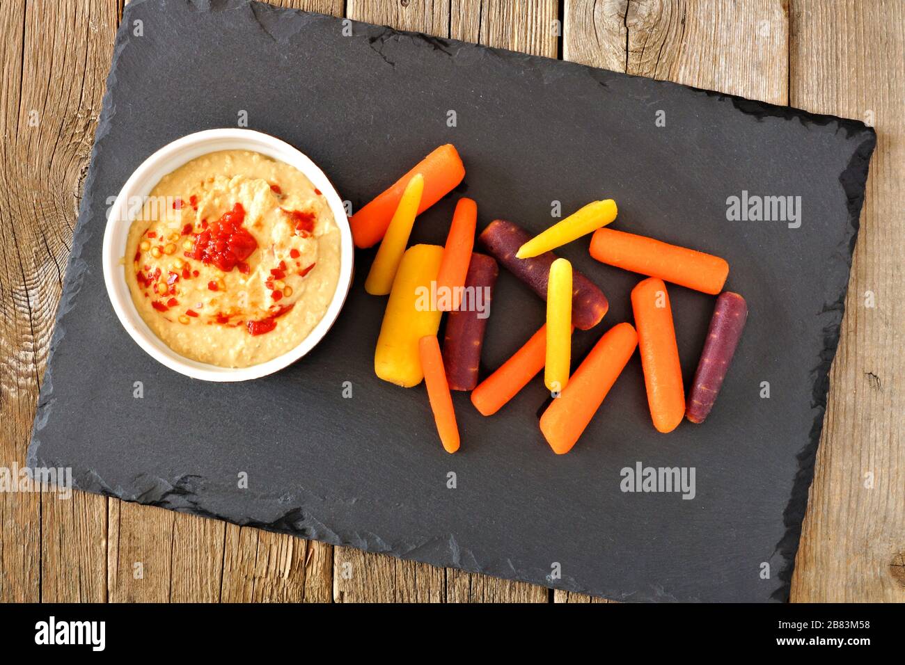 Baby rainbow carrots with hummus dip on a slate server over a rustic wooden background Stock Photo