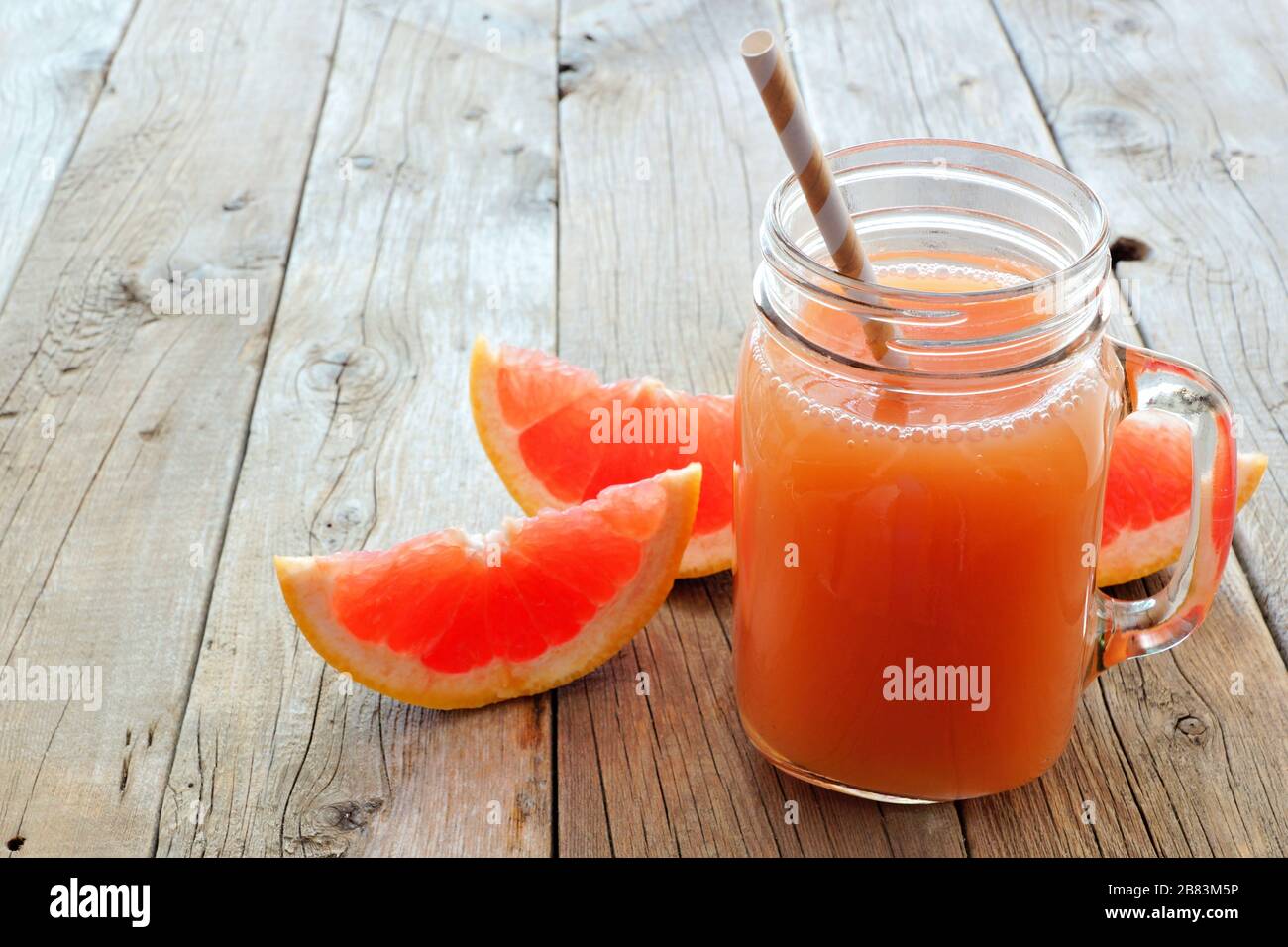 Mason jar glass of grapefruit juice with fruit slices and straws on rustic wooden background Stock Photo