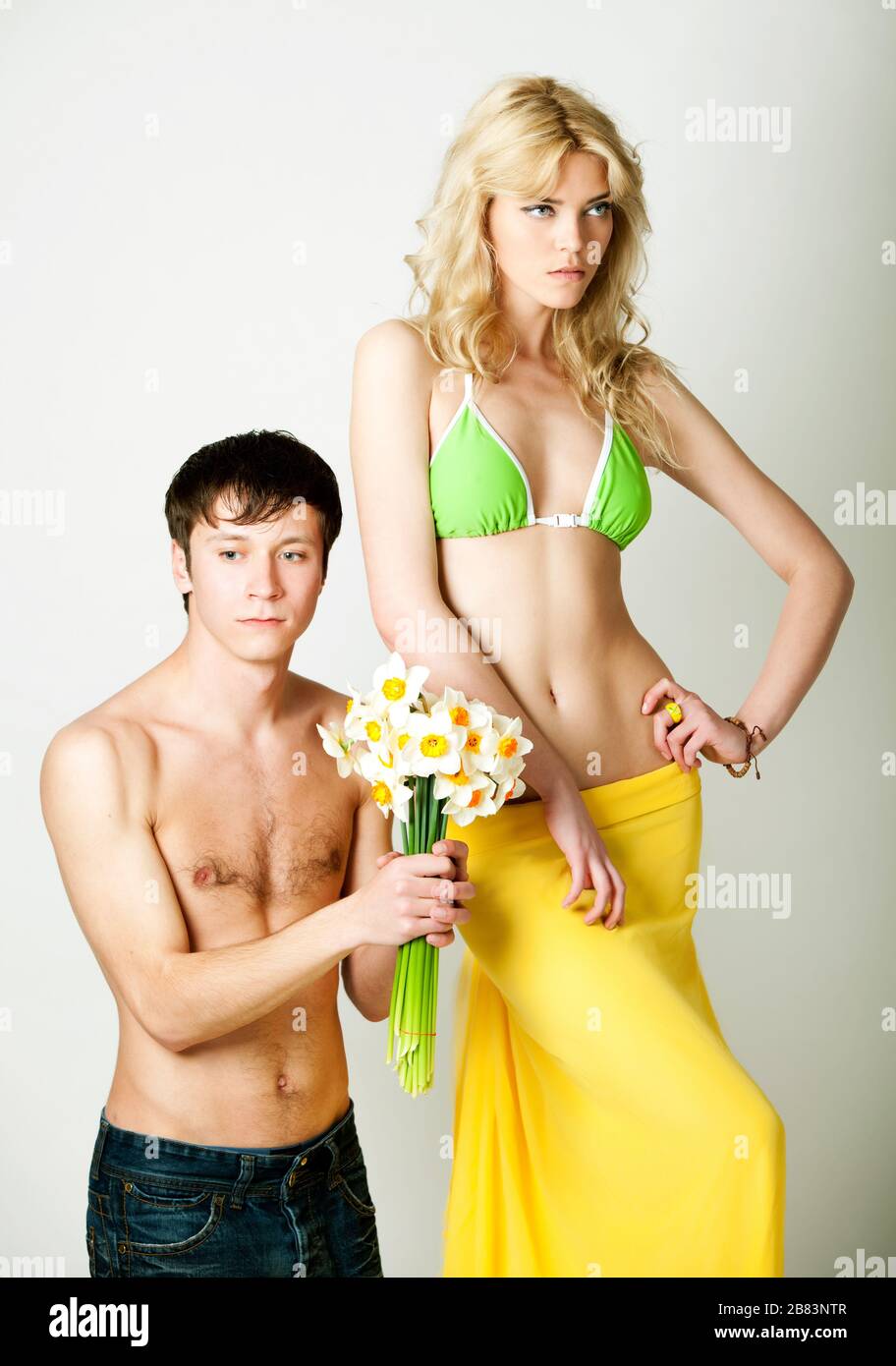 Young man presenting flowers to blond beautiful woman in green bikini and  yellow pareo over white background in photo studio. Beauty and fashion  lifes Stock Photo - Alamy