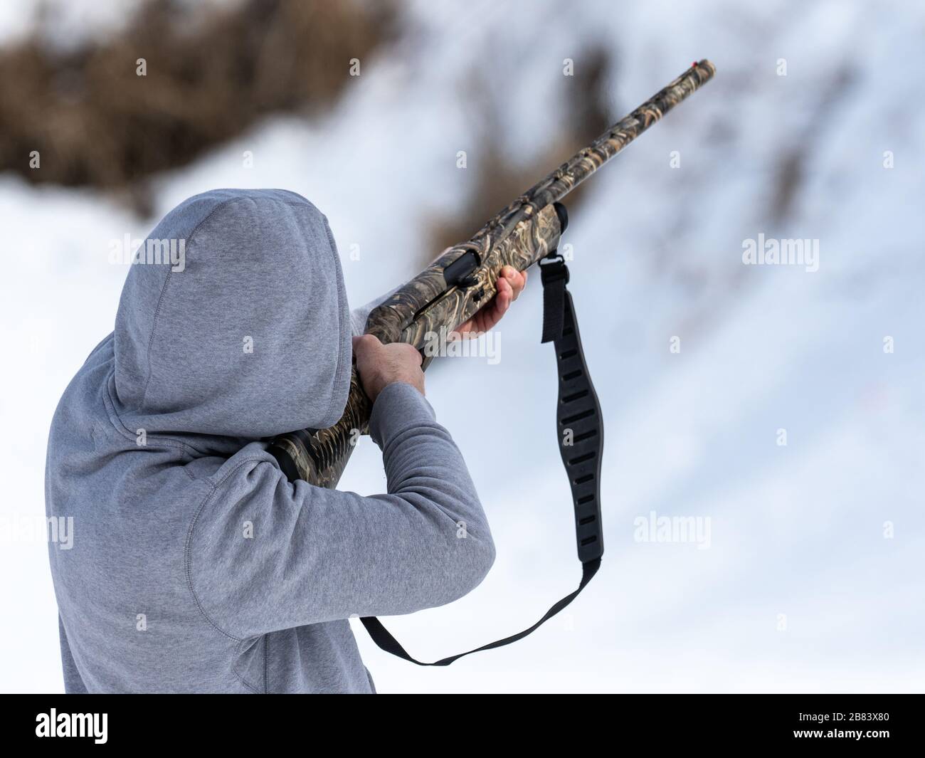 man in hoodie shooting with a camo shotgun Stock Photo
