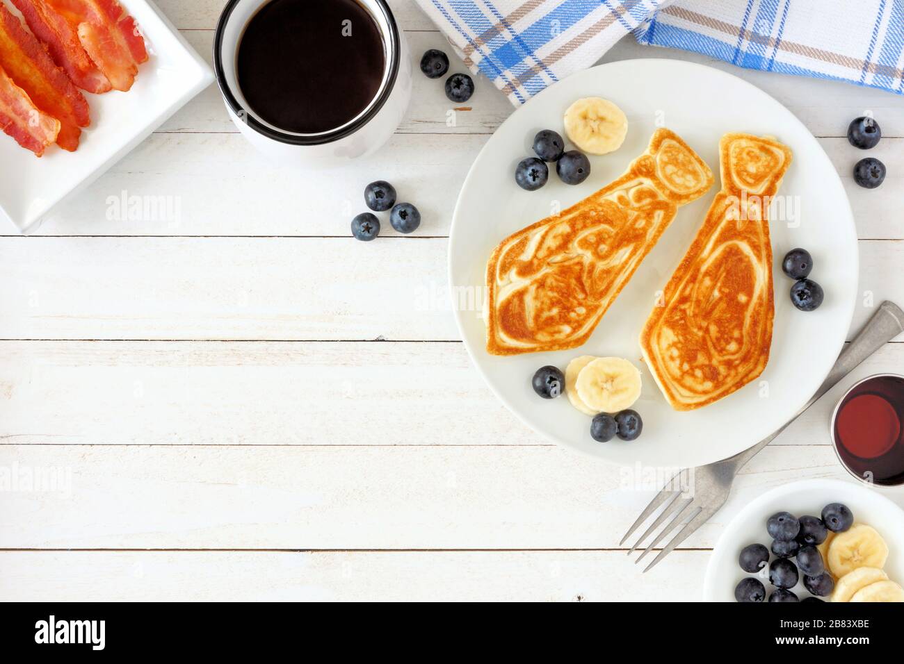 Tie shaped pancakes with blueberries and bananas. Fathers Day breakfast concept. Top view corner border on a white wood background. Stock Photo