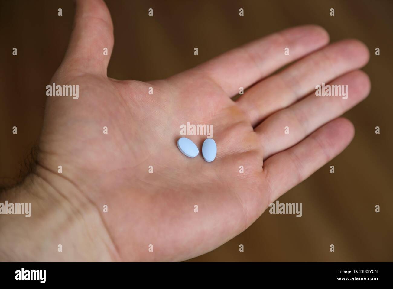 Two generic naproxen sodium pills, used as a nonsteroidal anti-inflammatory painkiller drug (NSAID), are shown held in a hand. Stock Photo