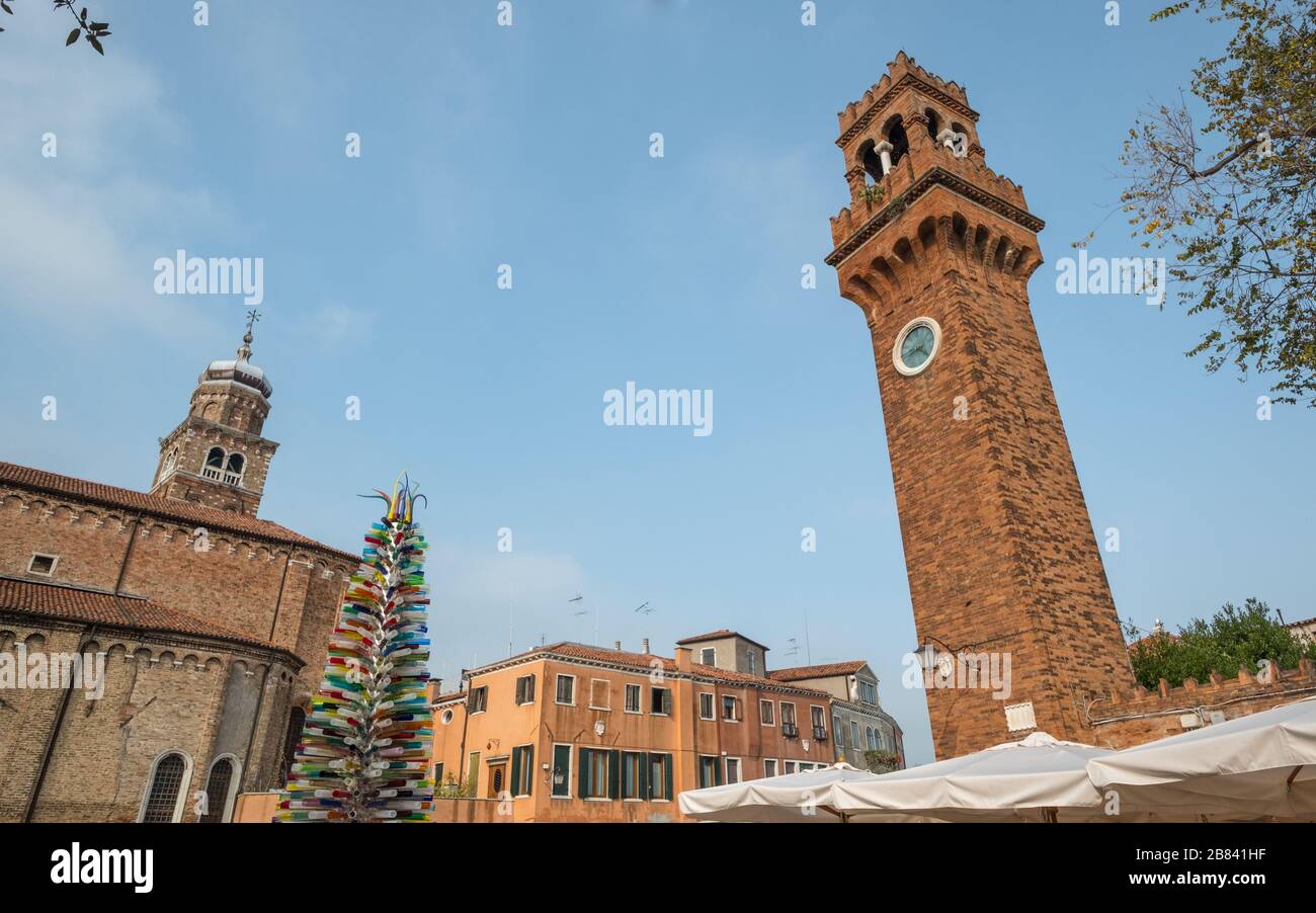 Looking up to Clock Tower beside Santo Stefano Church and bell tower of San Pietro Martire Church, Murano.  Tree of colored, blown glass cylinders Stock Photo