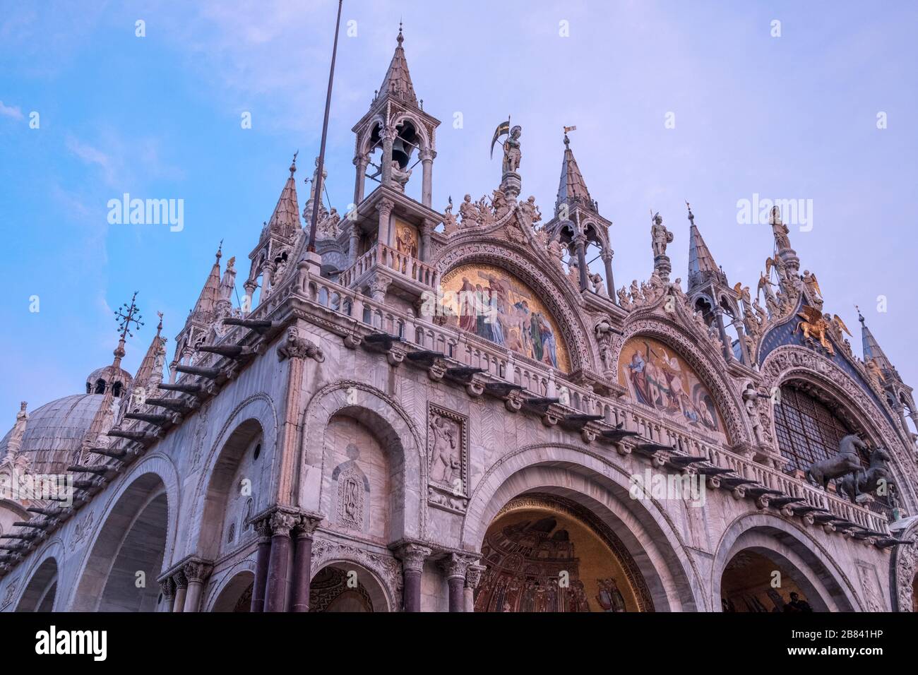Looking up to northwest corner of ornamented roofline of St Mark's Basilica, Venice. Marble glows pink with light from setting sun. Stock Photo