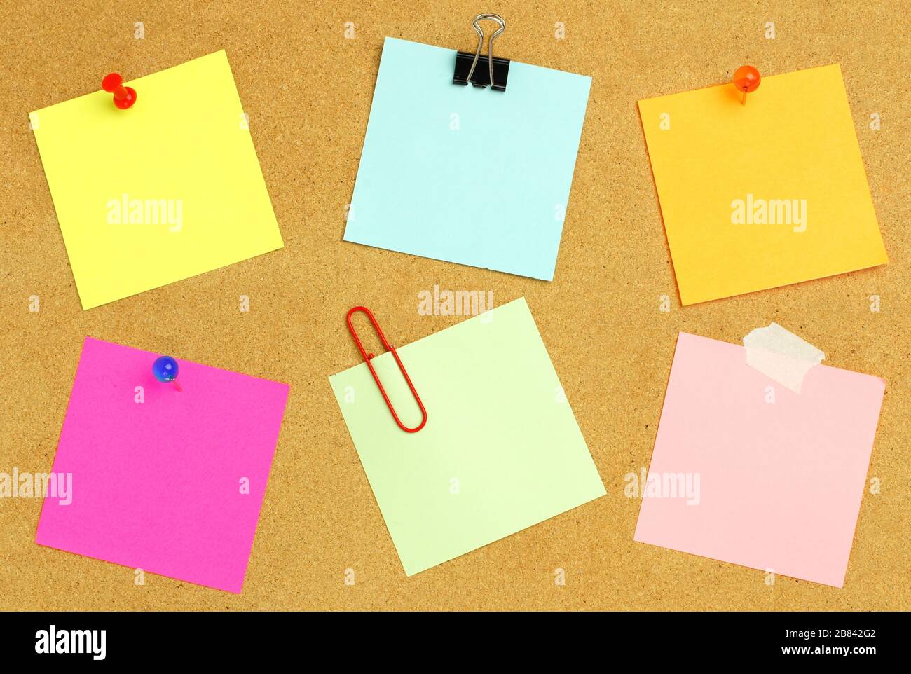 Blank sticky notes of various colors and fasteners on a bulletin board Stock Photo