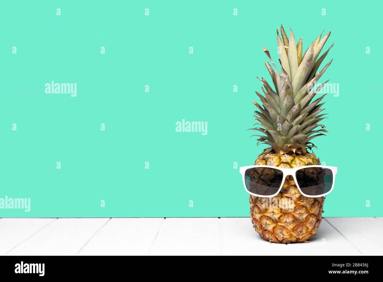 Hipster pineapple with sunglasses against a teal colored background. Minimal summer concept. Stock Photo