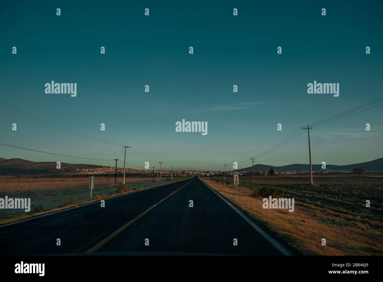 shot at sunset Highway leading to town in semi-arid landscape in the state of Hidalgo Stock Photo