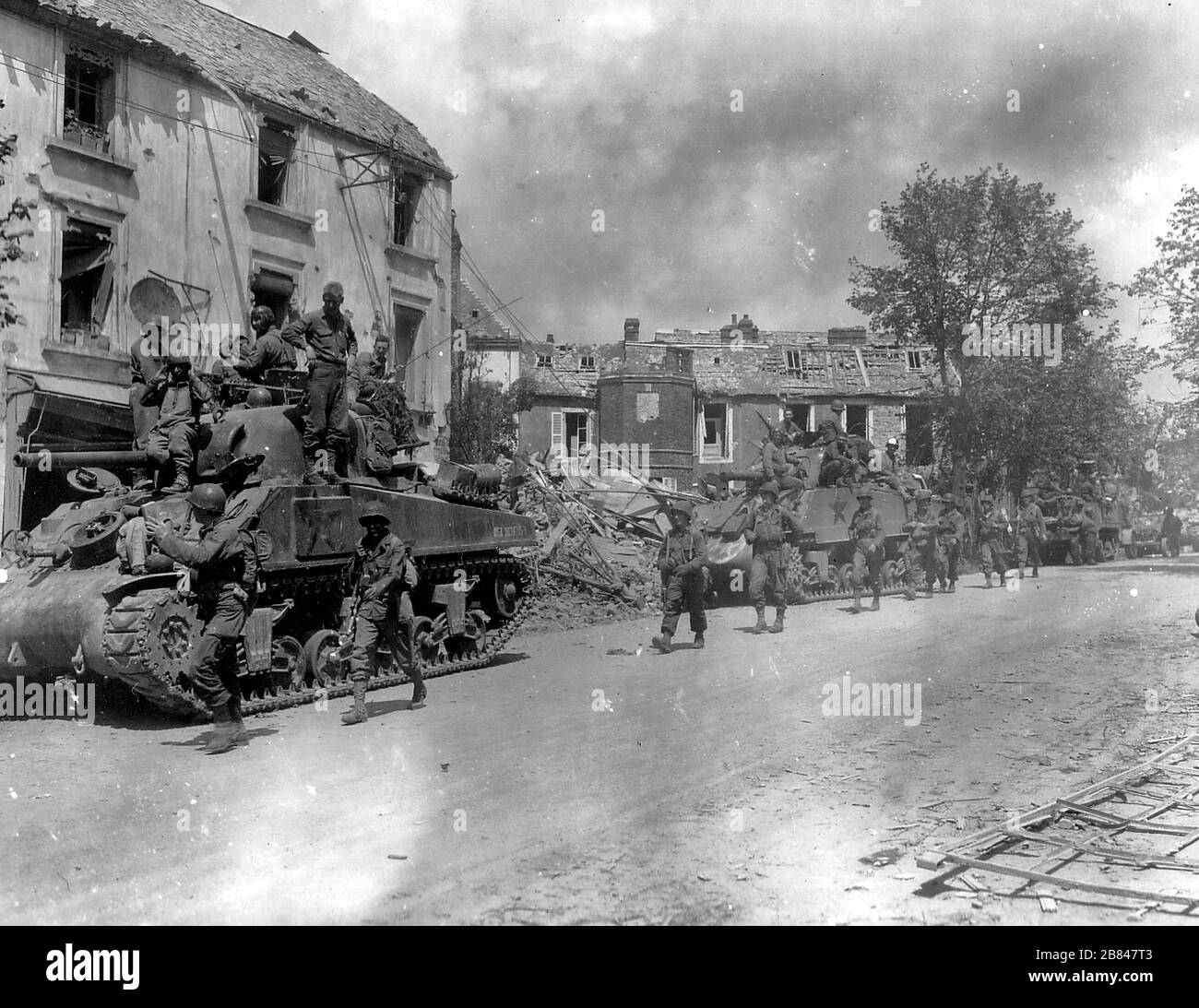American armored and infantry forces pass through the battered town of Coutances, France, in the new offensive against the Nazis. July 1944 Stock Photo