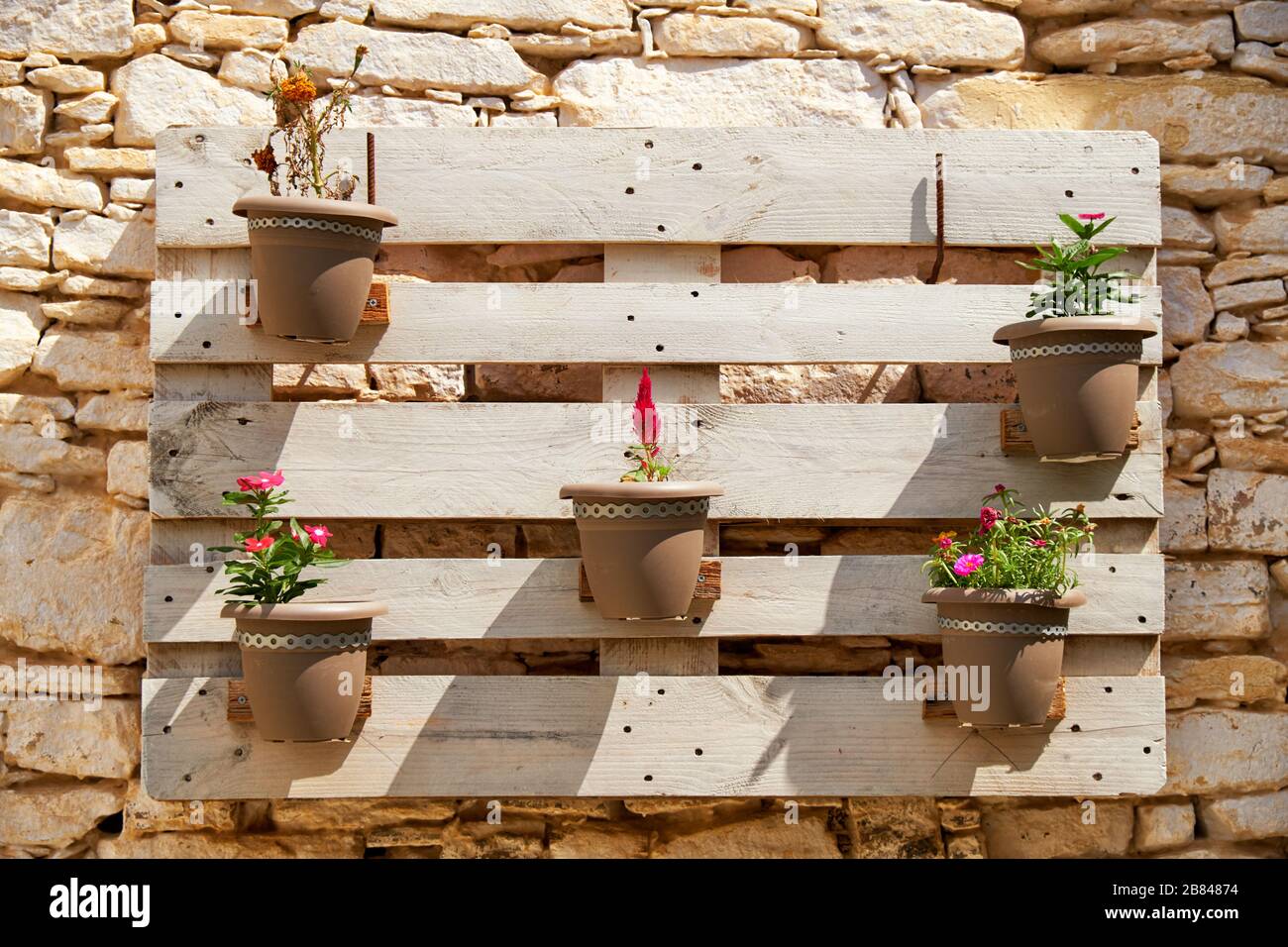 The decorative wooden shield pot plant holder with blooming flowers on the stone wall of old house in the Pano Lefkara village. Cyprus Stock Photo