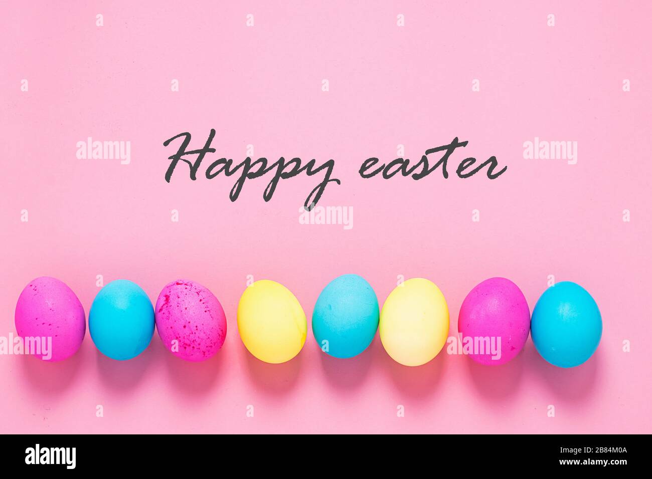 Colored eggs lie in a row on a pink background text Happy Easter. Festive spring concept. Copy space flat lay banner Stock Photo