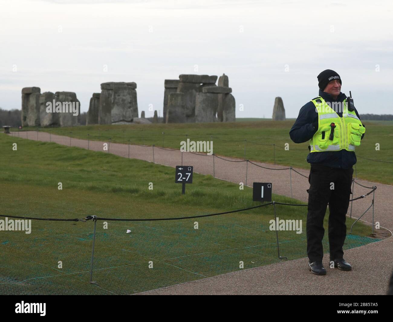 A security guard stands on a footpath near Stonehenge on Salisbury Plain in Wiltshire, where the traditional equinox celebrations inside the stones were cancelled after English Heritage, which manages the attraction, closed the site until May 1 following government advice on coronavirus. Stock Photo