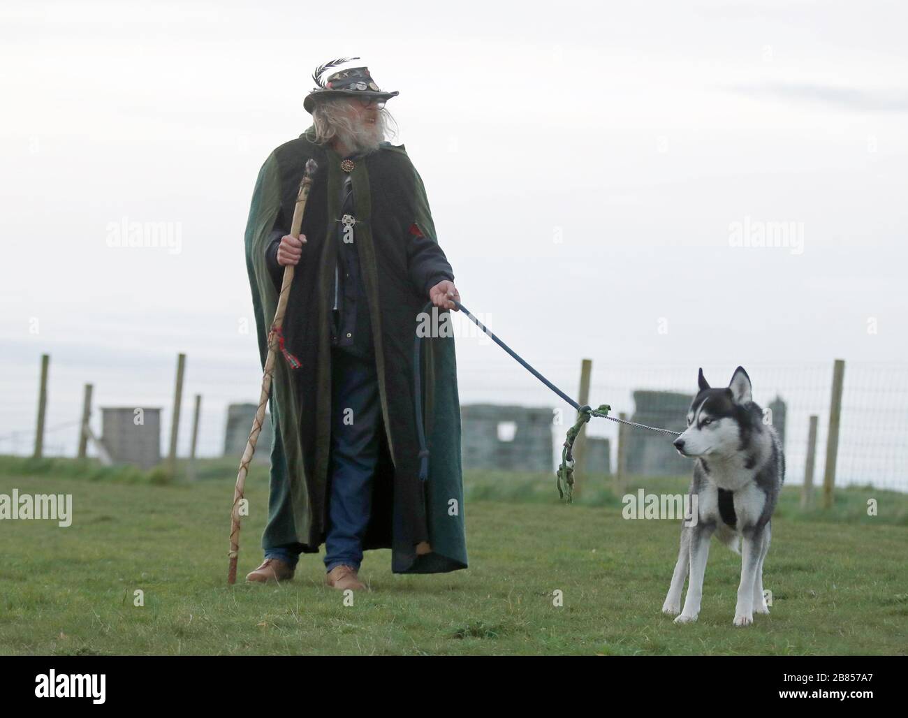 A man with a dog stands near Stonehenge on Salisbury Plain in Wiltshire, where the traditional equinox celebrations inside the stones were cancelled after English Heritage, which manages the attraction, closed the site until May 1 following government advice on coronavirus. Stock Photo