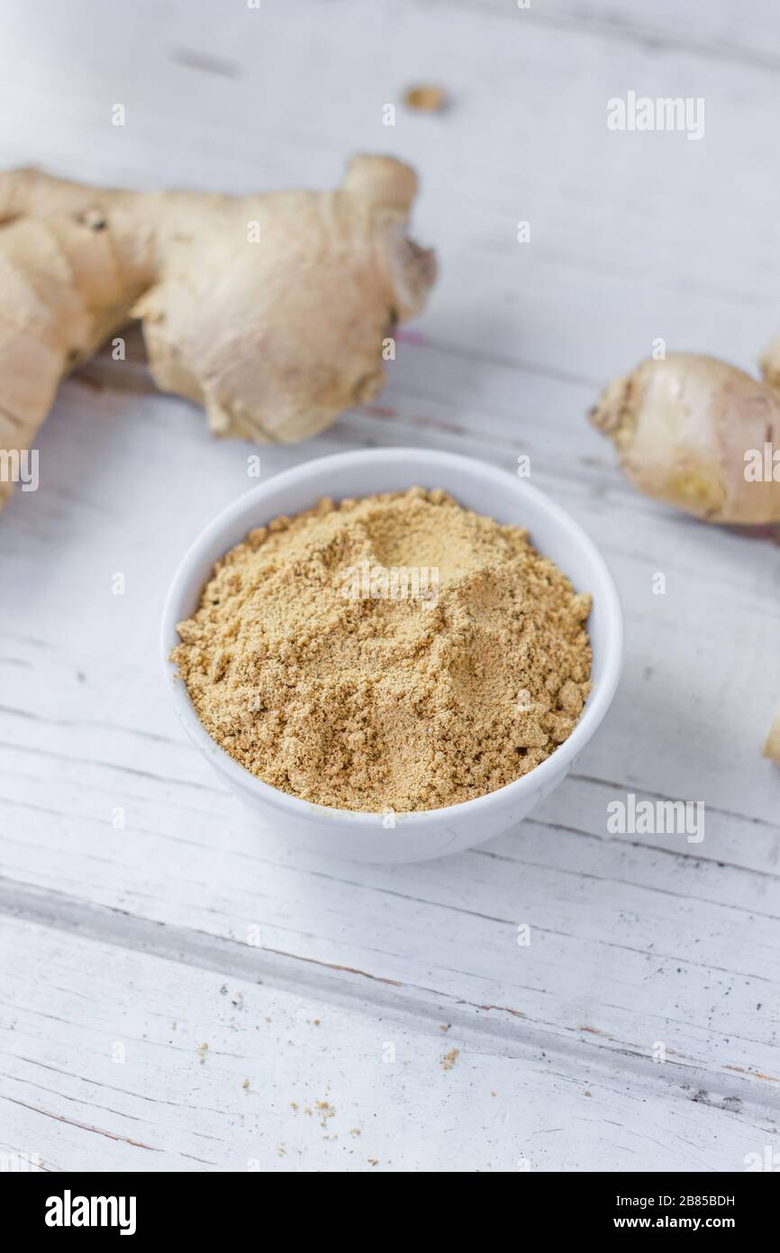 Grounded ginger and ginger root on white wooden surface. Stock Photo