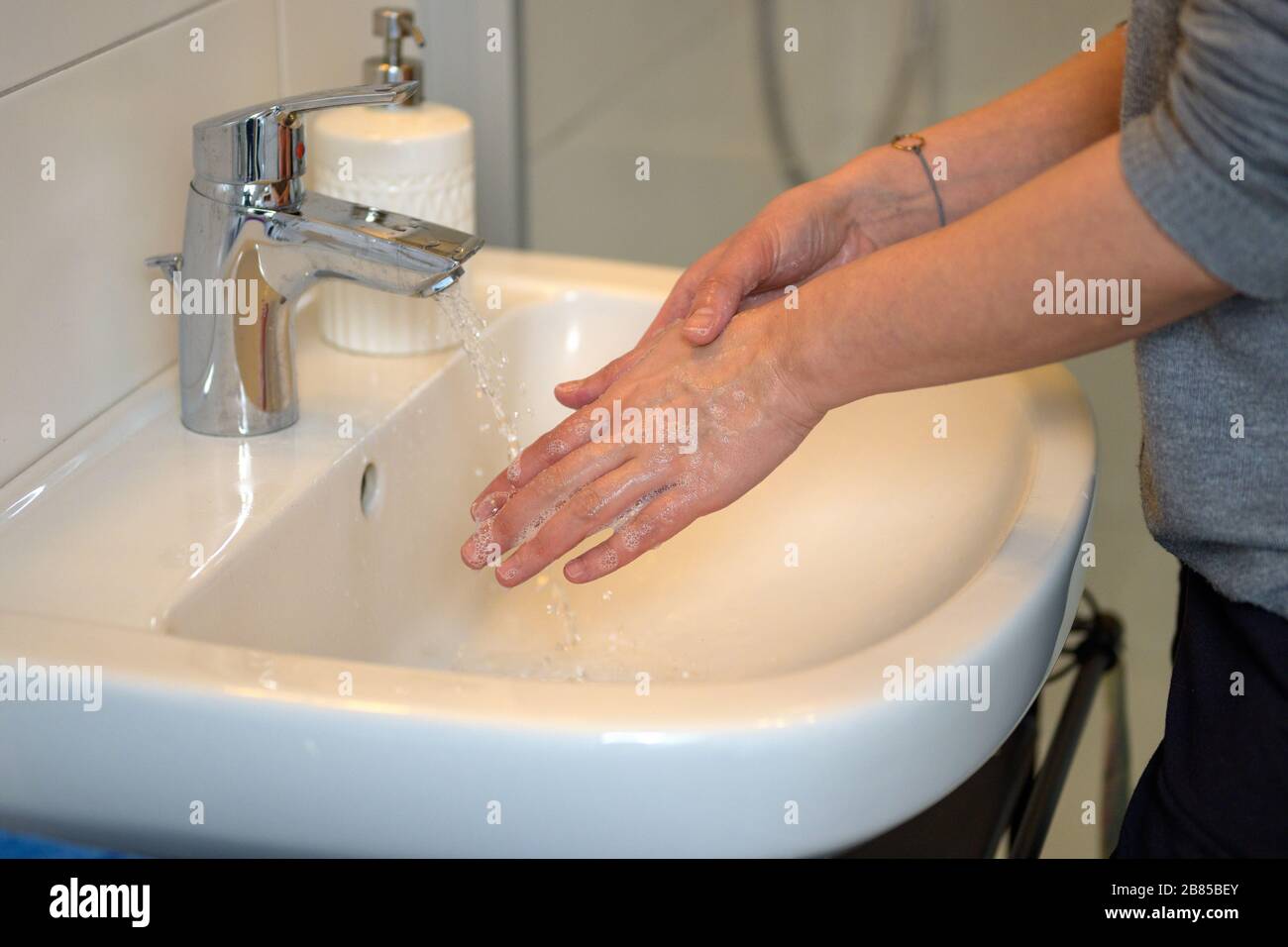 Woman washing her hands under running water over a hand basin in a bathroom in a personal hygiene concept Stock Photo