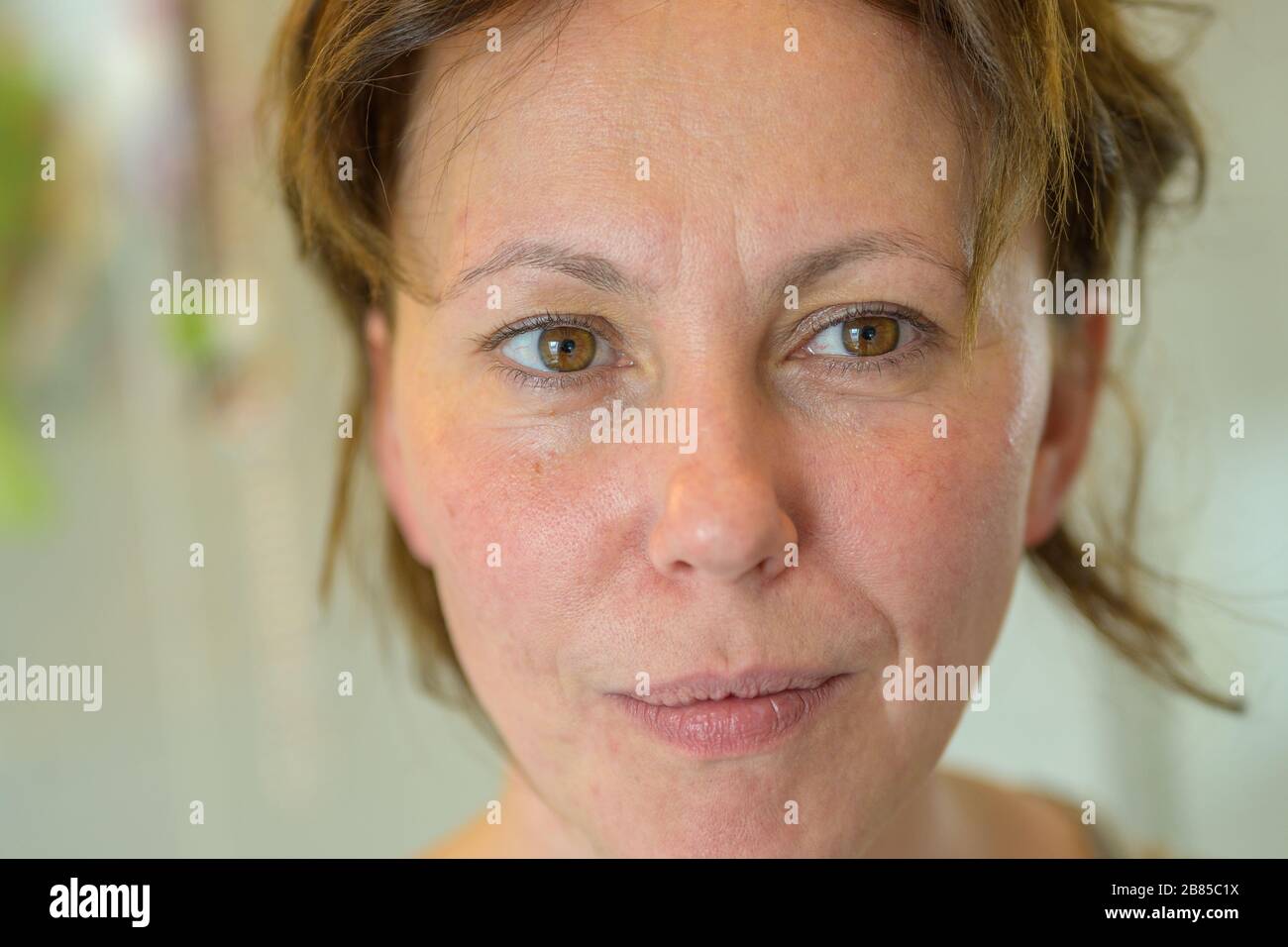 Serious woman with a quiet pensive smile glancing to the side in a close up cropped facial portrait indoors Stock Photo