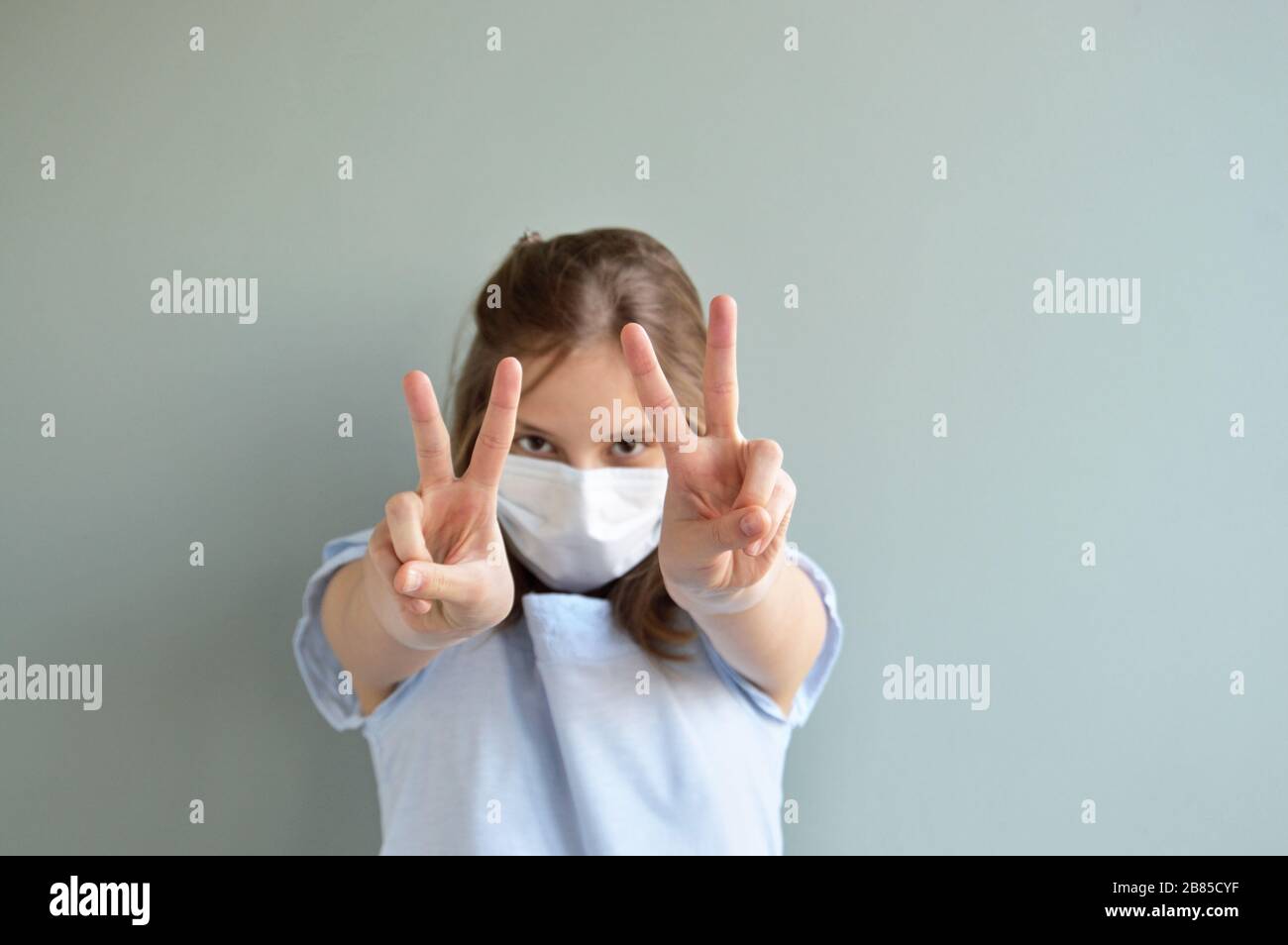 Victory sign shown by girl wearing surgical mask Stock Photo