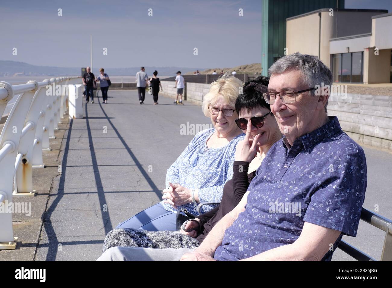 Mother, Father and daughter sat on a bench on the promenade, looking out to sea on a day out Stock Photo