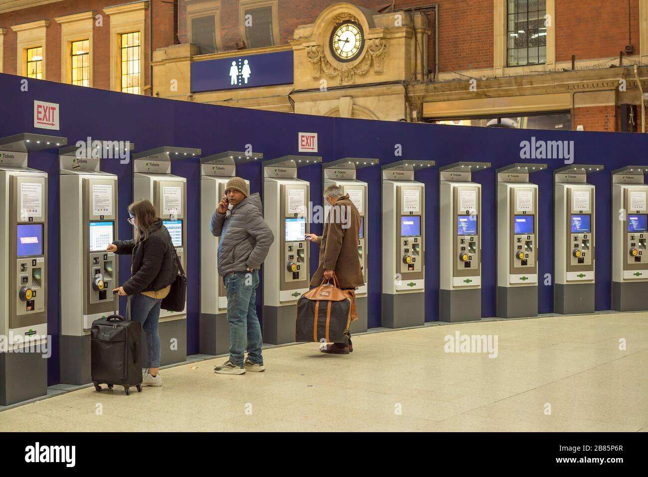 Rail passengers buying train tickets at automatic machines, Victoria train station, London UK, at night. London transport, rail travel, ticket machine. Stock Photo