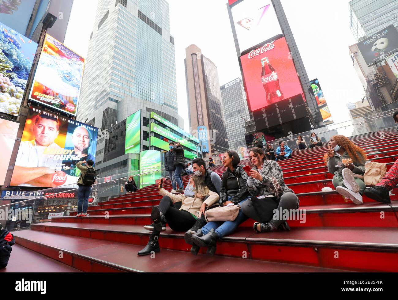 New York, USA. 19th Mar, 2020. Tourists wearing facial masks sit on the red stairs on Times Square in New York City, the United States, March 19, 2020. The number of COVID-19 cases in the United States topped 13,000 as of 5:30 p.m. (2130 GMT) on Thursday, according to the Center for Systems Science and Engineering (CSSE) at Johns Hopkins University. The fresh figure reached 13,060 with 175 deaths. Credit: Wang Ying/Xinhua/Alamy Live News Stock Photo