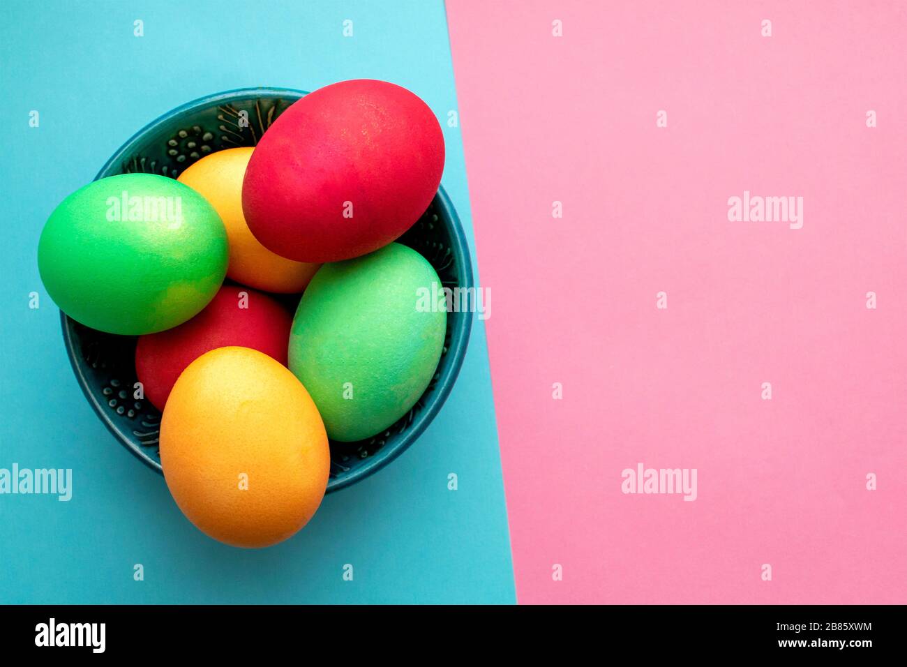 Dyed Easter eggs in a blue bowl on mixed pink and blue background with copy space. Symbol of main Christian feast celebration. Easter decoration backg Stock Photo