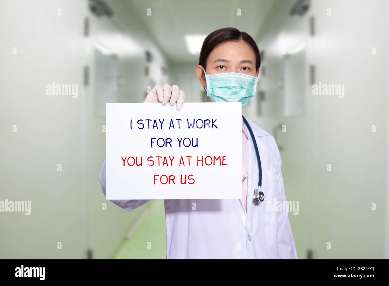 Asian doctor at hospital wear medical masks, holding paper with text I STAY AT WORK FOR YOU, YOU STAY AT HOME FOR US. stay at home policy campaign to Stock Photo