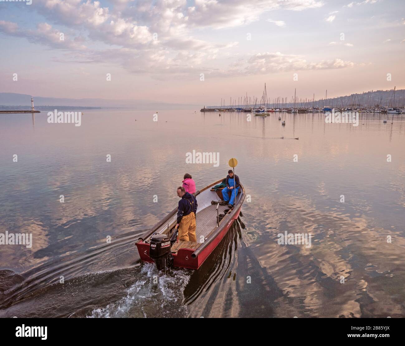 Fishermen leave to collect catches from pots. Sunrise over lake Geneva as the crew and their small boat head out from shore to check their catch Stock Photo