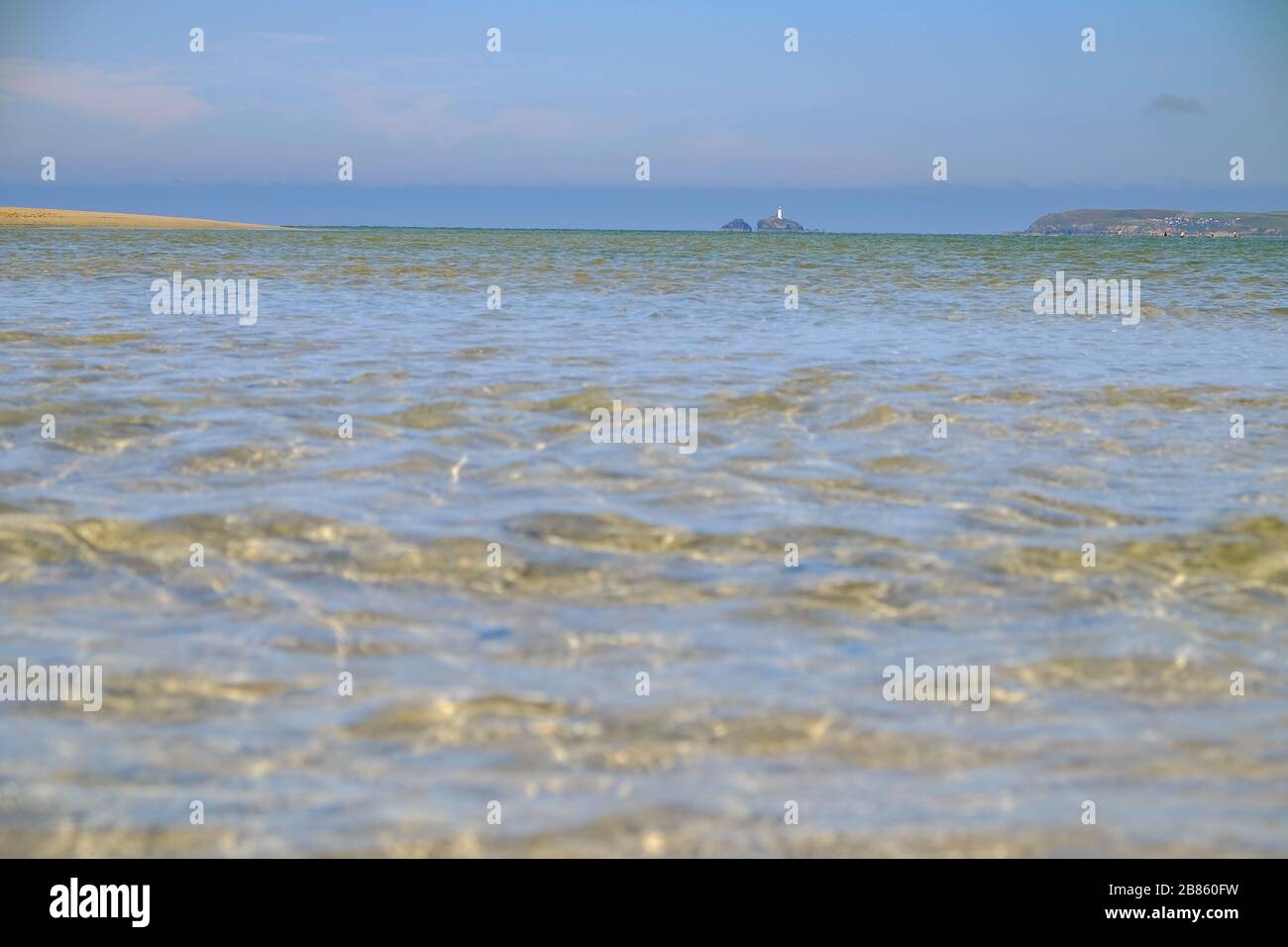 Low shot of rippling green blue sea in the foreground with sandy beach and lighthouse in the background Stock Photo