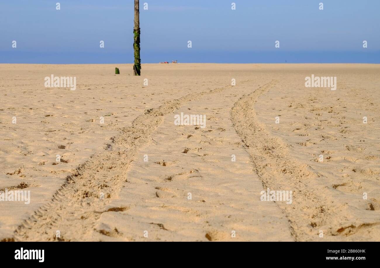 Tyre tracks in the golden sand with blue sea and sky in the background Stock Photo