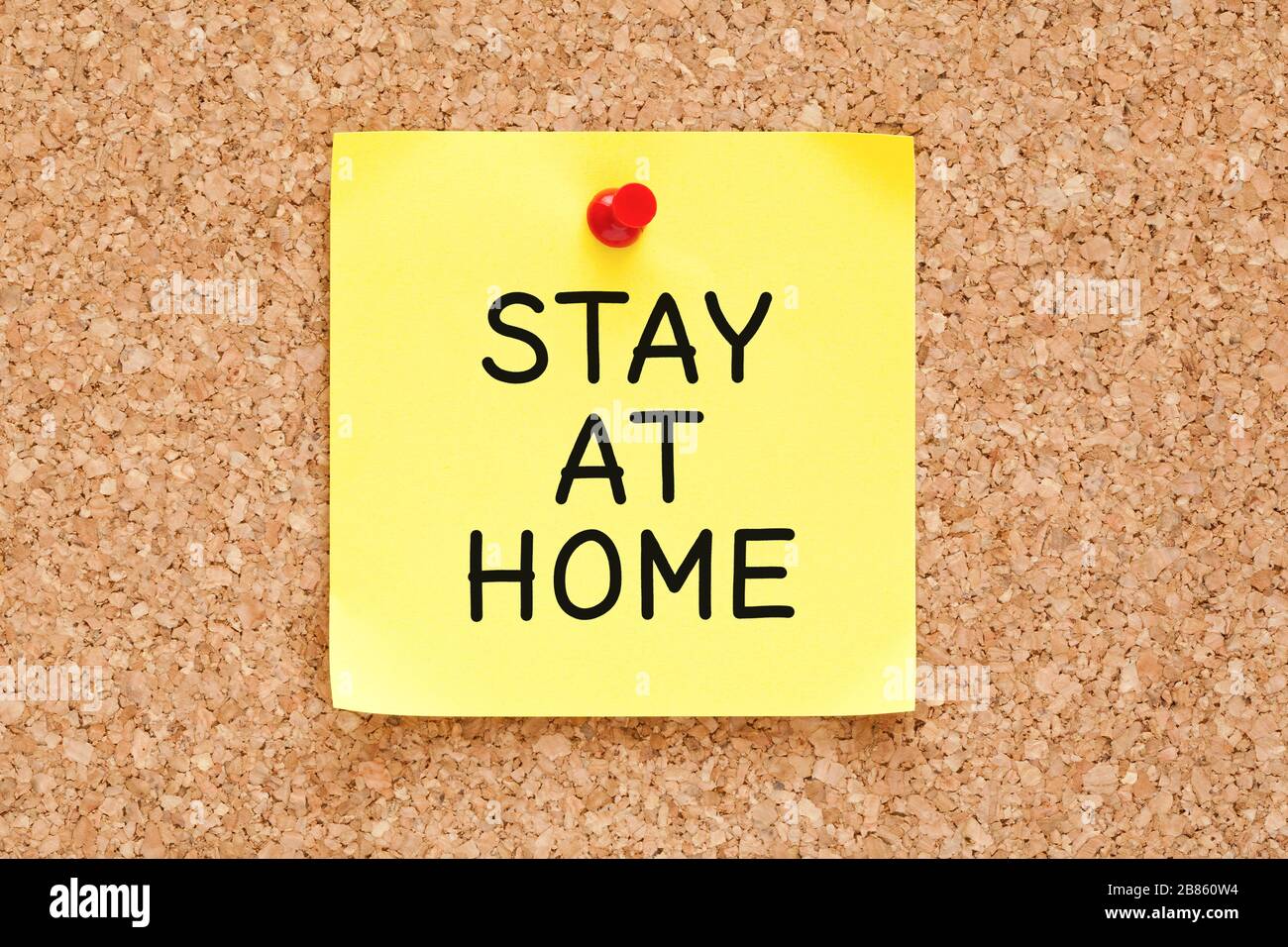 Text Stay at Home handwritten on yellow sticky note pinned on cork bulletin board. Social Distancing and Self-isolation concept. Stock Photo