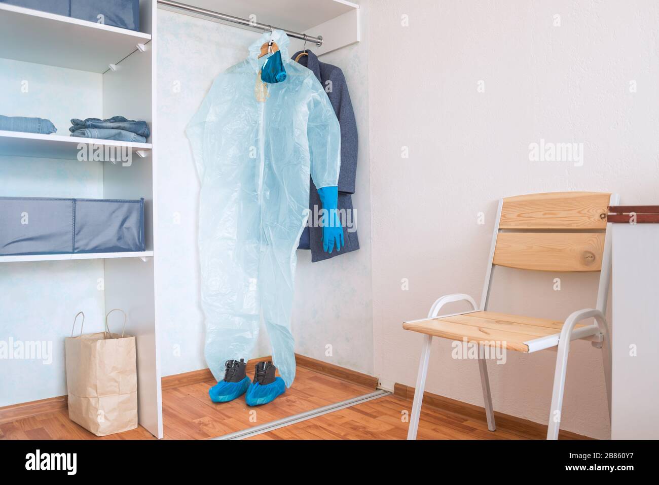 protective suit with gloves, mask and glasses hanging in wardrobe with otherclothes at over reacting and panicing person's home Stock Photo