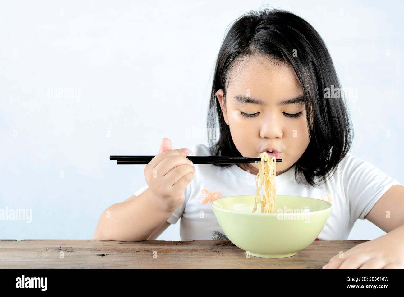 Asian girls are blowing instant noodles with a lot of appetite. With her sweat on the forehead, She looks cute and appetizing, a happy child. Stock Photo