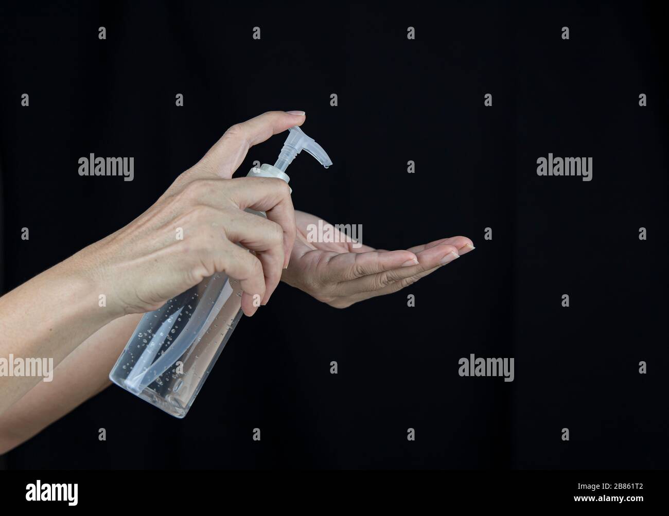 A female with a hand sanitizer push gel in hand on black background. Stock Photo