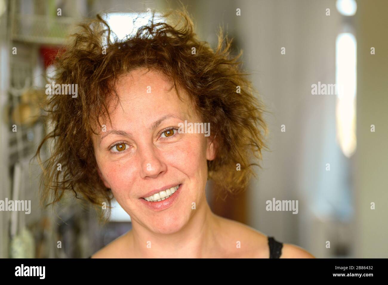 Attractive natural Hispanic woman with curly unruly hair giving the camera a quiet smile on a bad hair day indoors at home Stock Photo