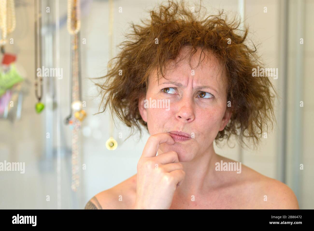 Thoughtful charismatic woman assessing her unruly tousled hair on a bad hair day looking up at it with a frown and finger to mouth Stock Photo