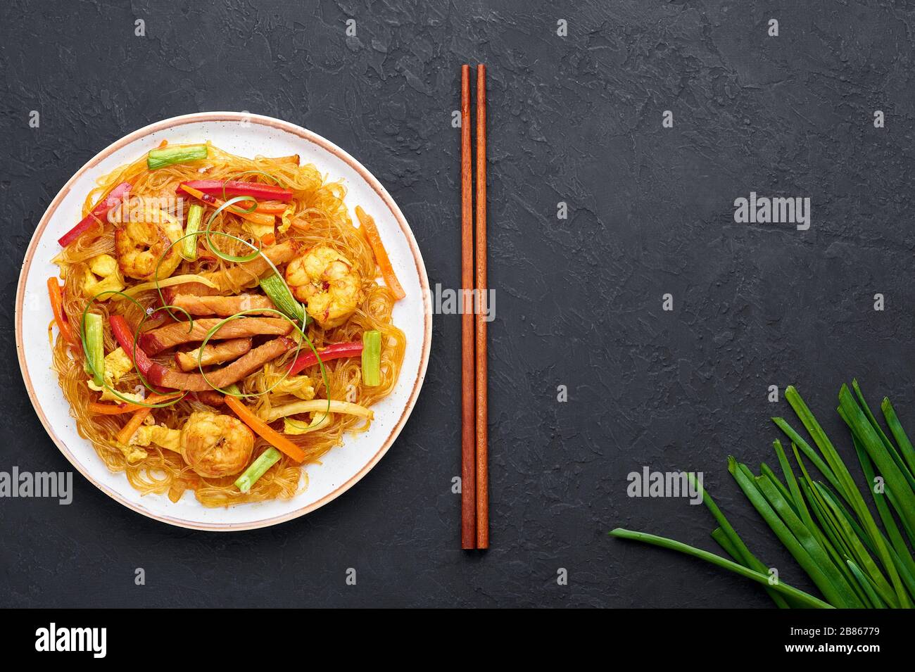 Singapore Mei Fun in white plate on dark slate background. Singapore Noodles is chinese cuisine dish with rice noodles, prawns, char siu pork, carrot, Stock Photo