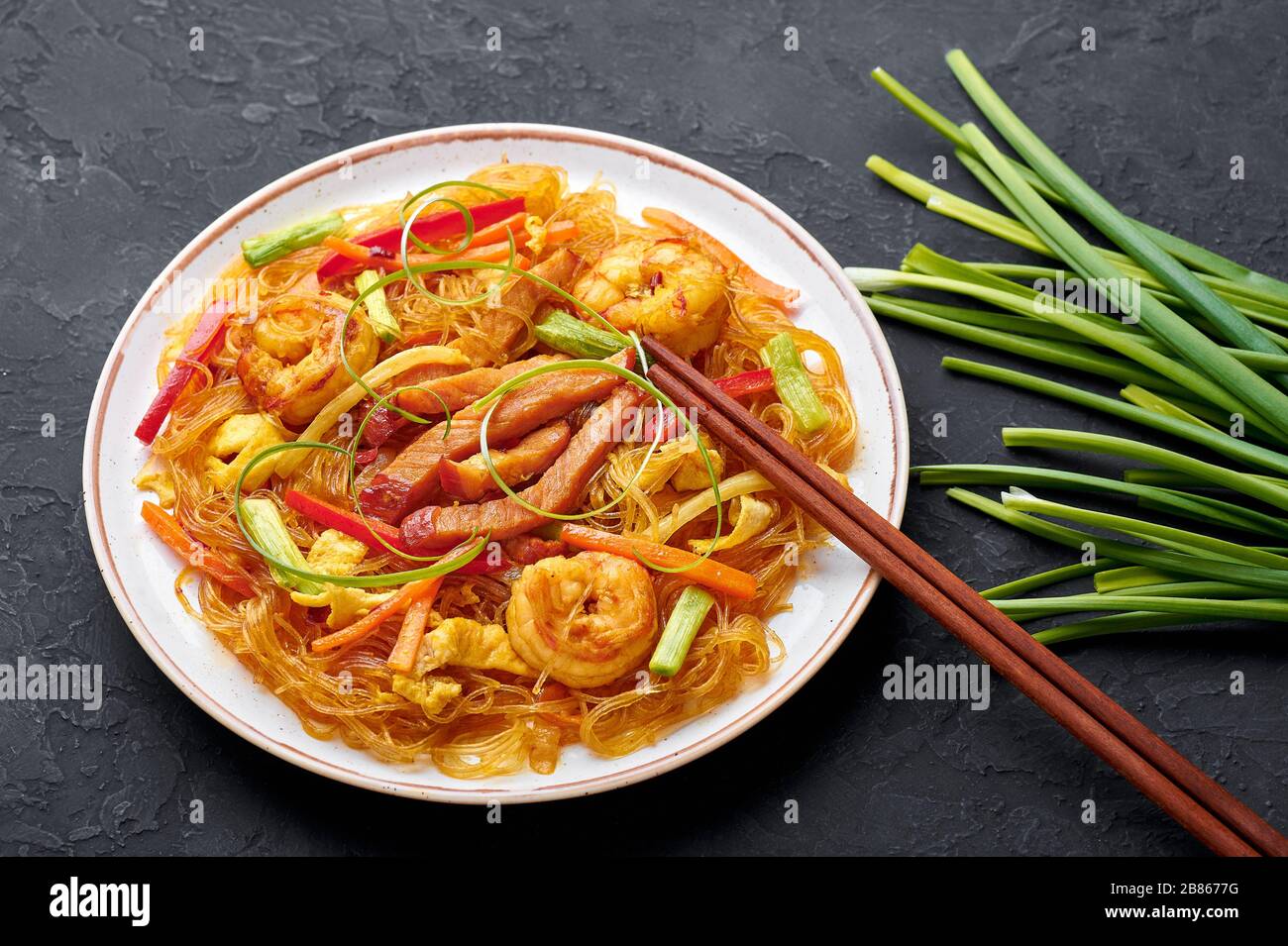 Singapore Mei Fun in white plate on dark slate background. Singapore Noodles is chinese cuisine dish with rice noodles, prawns, char siu pork, carrot, Stock Photo