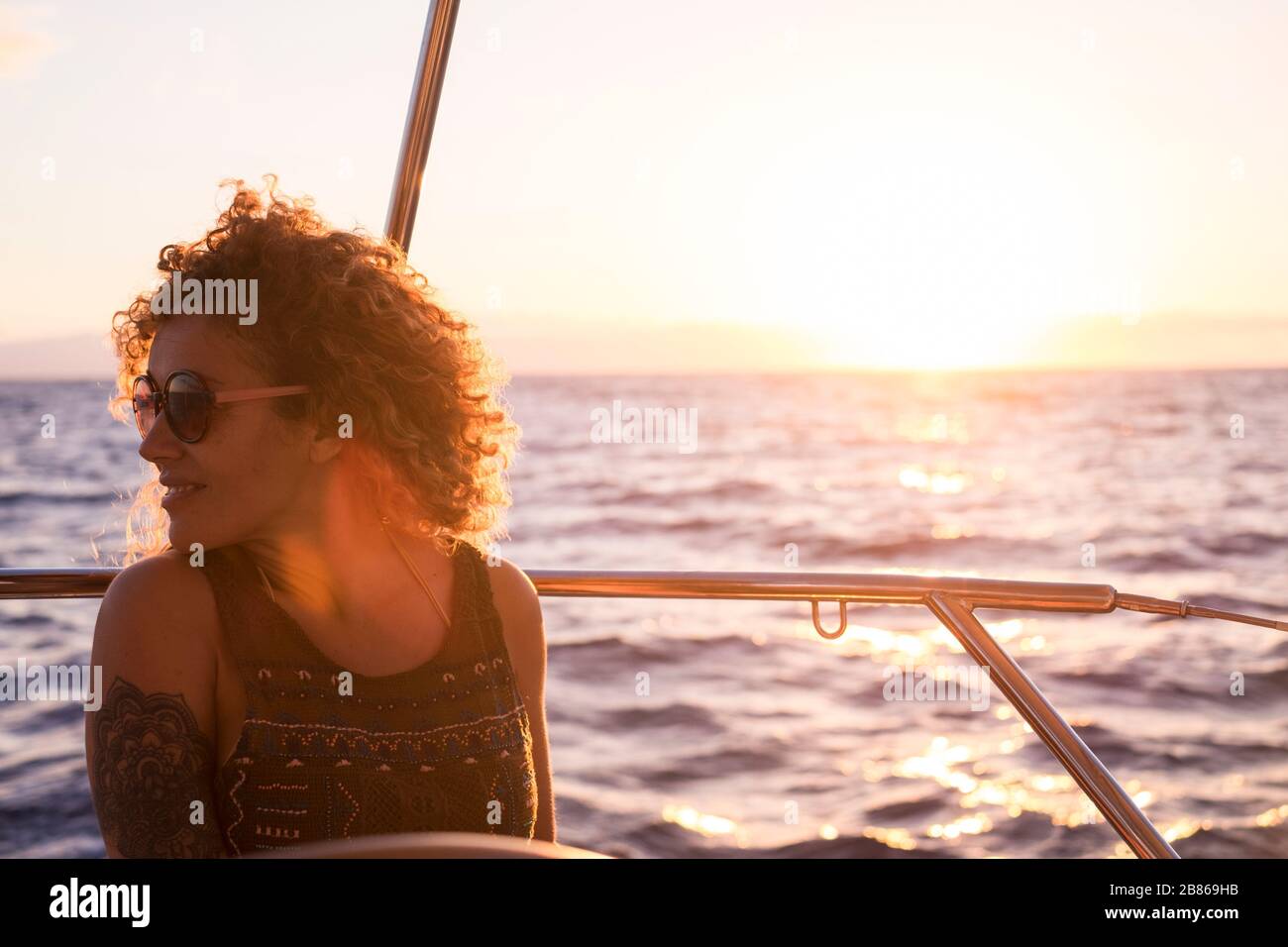 Sunset portrait of beautiful long hair caucasian woman on a sail boat enjoying the feeilng and the freedom with ocean around and sun in backlight - lu Stock Photo