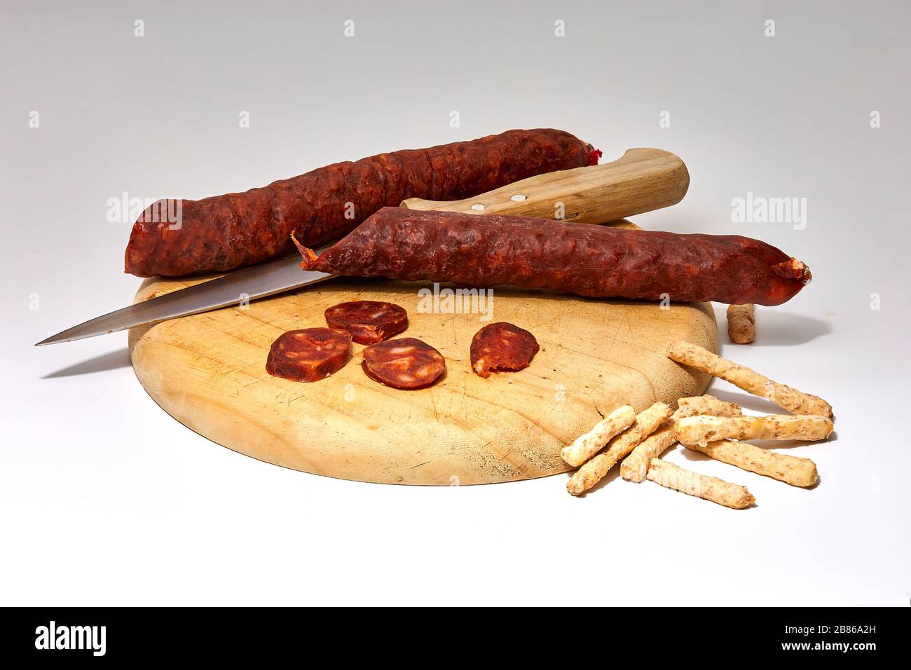 still life of cut sausage on wooden board with knife and white background Stock Photo