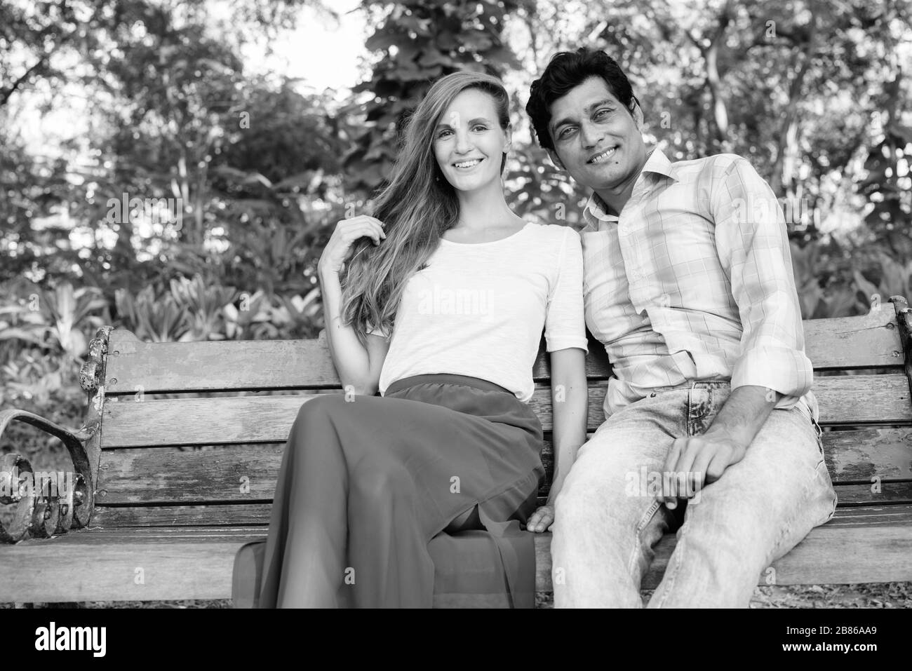 Happy multi ethnic couple smiling and sitting on wooden bench in love at the park Stock Photo