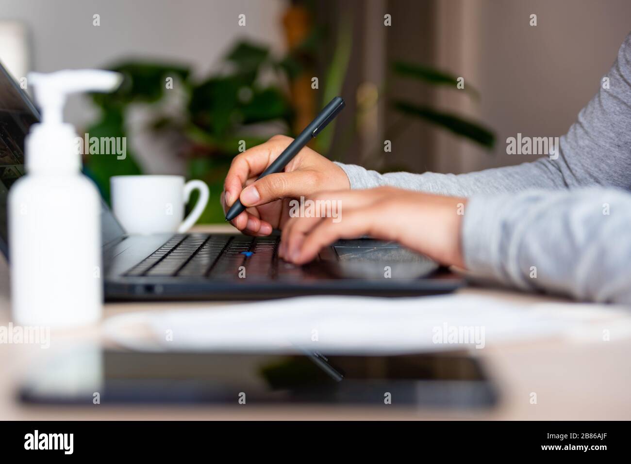close up of hands of young woman typing on laptop keyboard with hand sanitizer while remote working due to corona virus spread Stock Photo