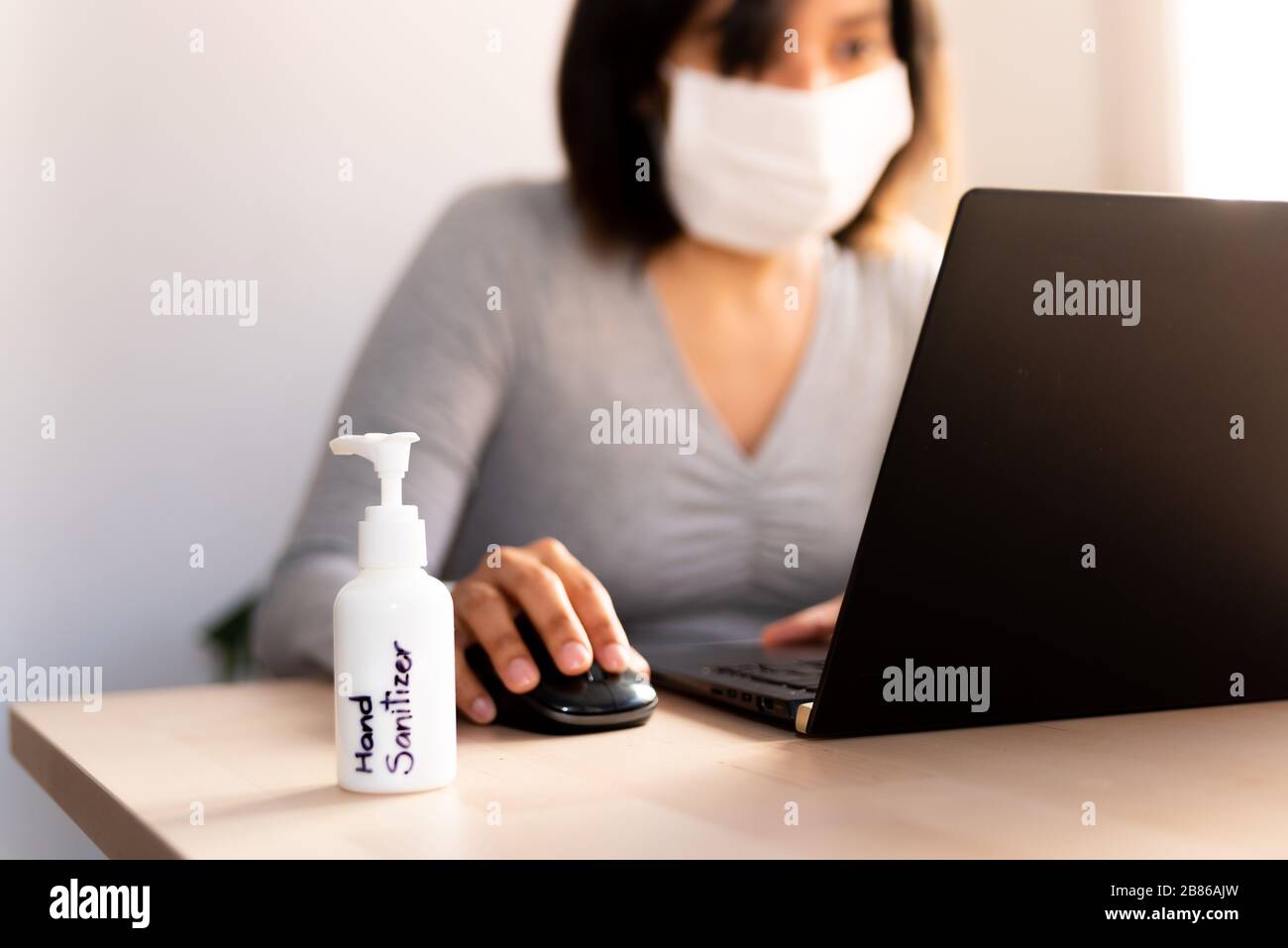 close up of hand sanitizer on wooden desk of a young woman doing remote work from home office due to covid19 virus contagion Stock Photo