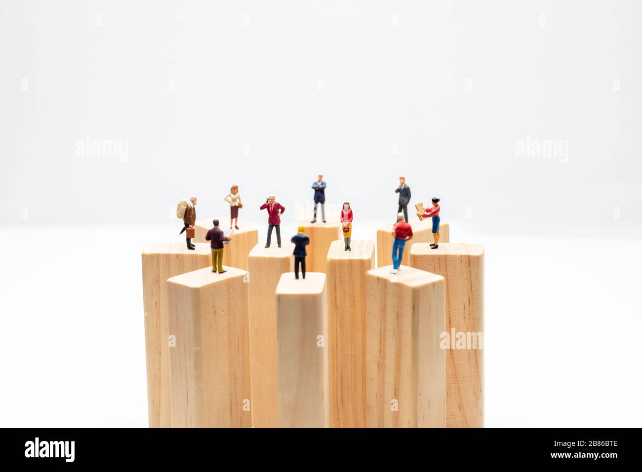 Miniature toys standing on wooden block - social distancing, anti-social or team work concept. Stock Photo