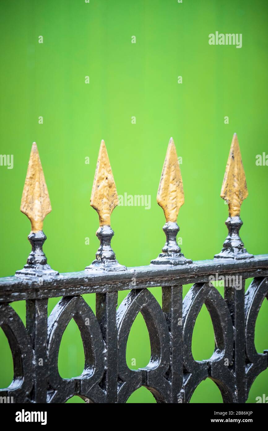 Gold painted spikes on a black wrought iron gate, with a green background Stock Photo