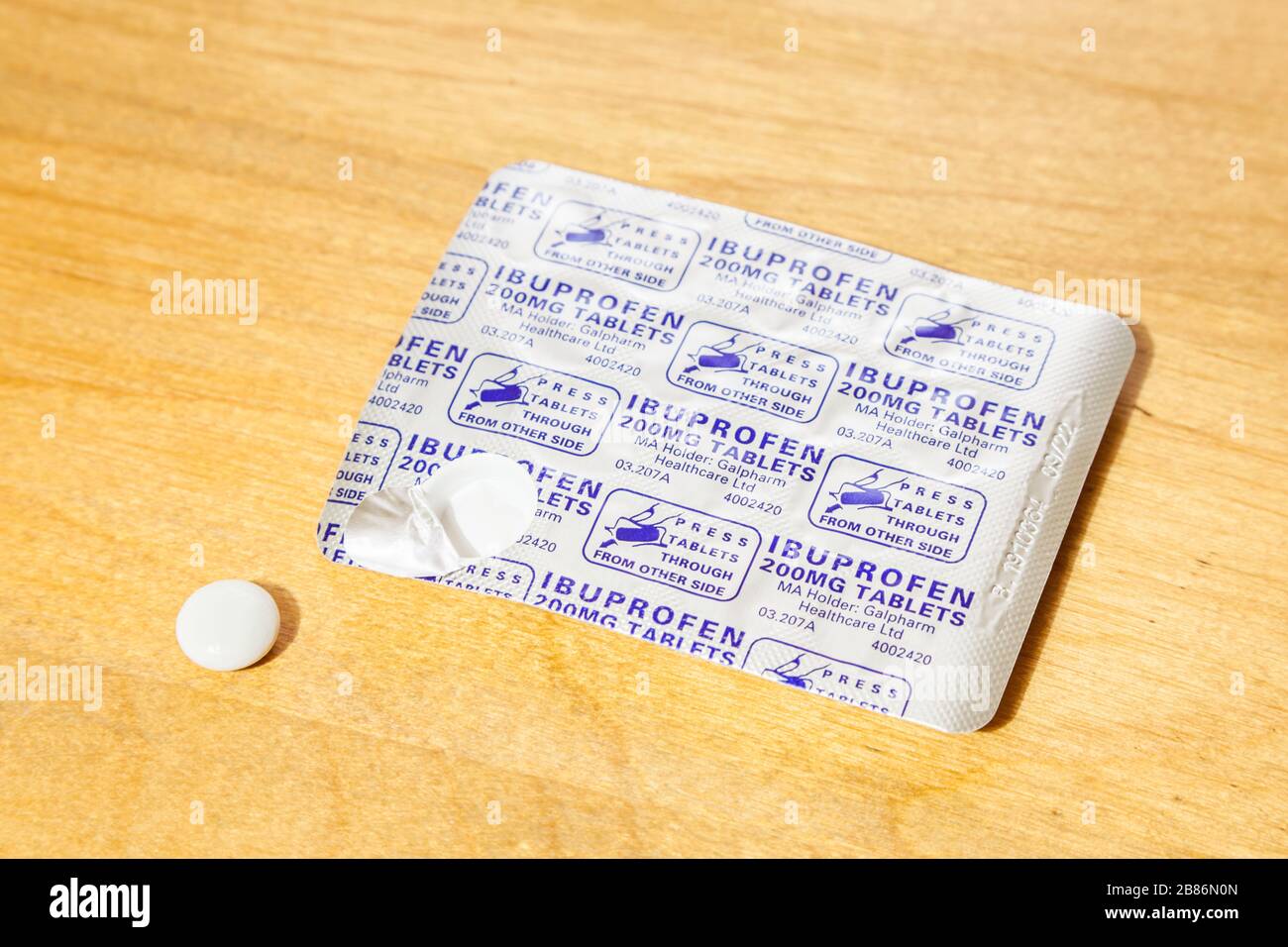 Pain relief pills. Ibuprofen 200mg tablets in a blister pack with one tablet removed from the packet and placed on a wooden table Stock Photo