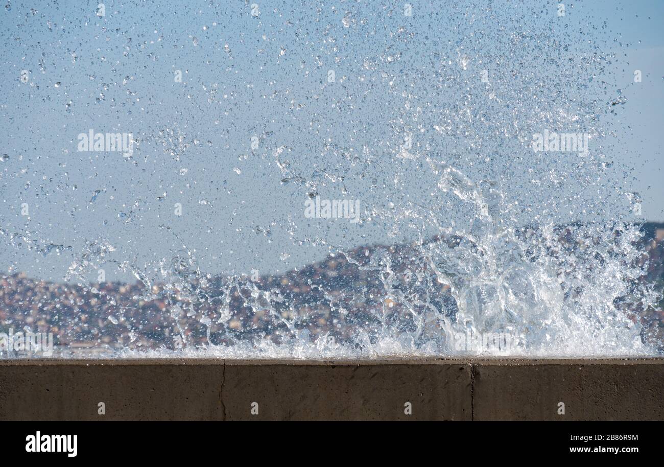 Waves hit the hard surface of concrete wall and splashing sea water. Stock Photo
