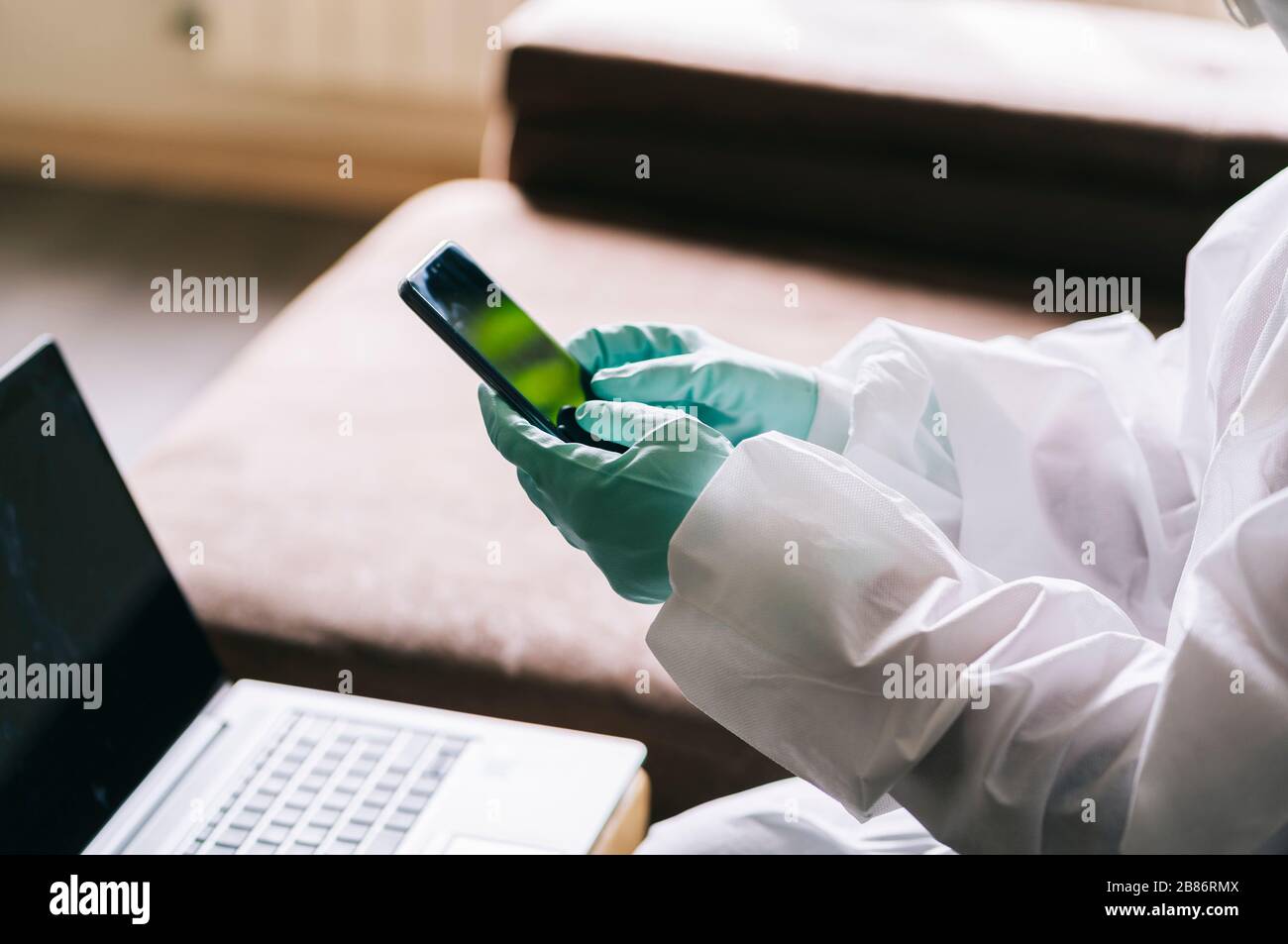 The hands of a person using the mobile phone with gloves and a safety suit against a pandemic or virus Stock Photo