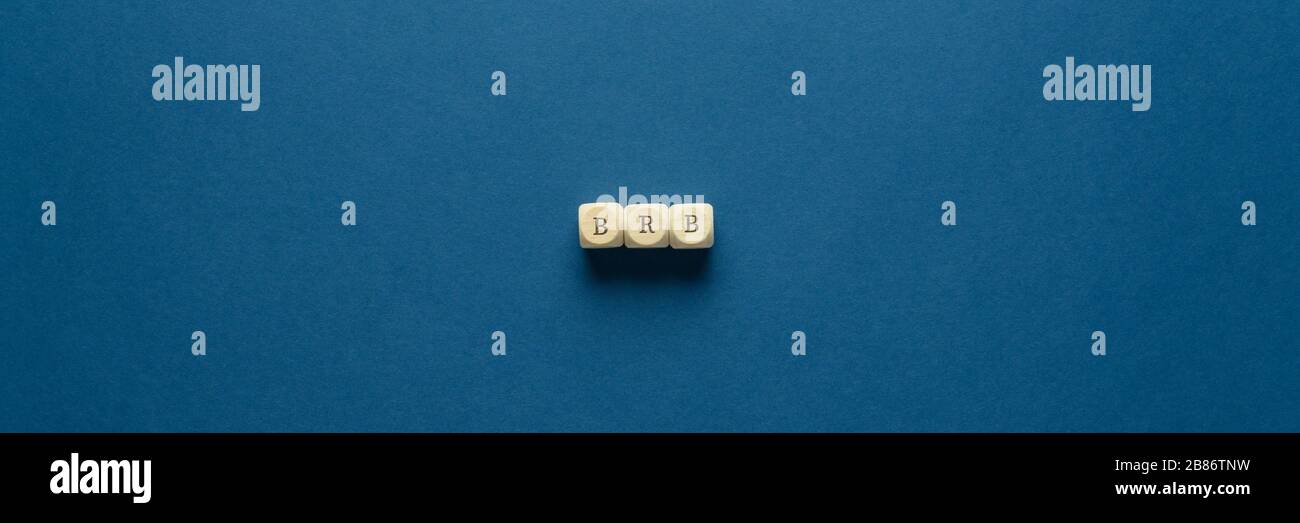 Wide view image of BRB abbreviation spelled on wooden dices. Placed over navy blue background. Stock Photo