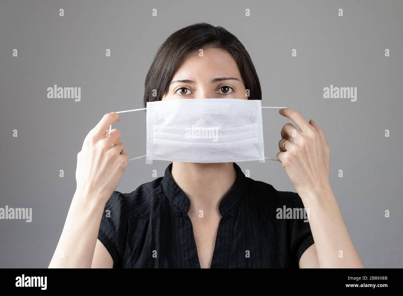 Brunette woman wearing hygienic mask to prevent infection, airborne respiratory illness such as flu, 2019-nCoV on gray background. Healthcare concept. Stock Photo