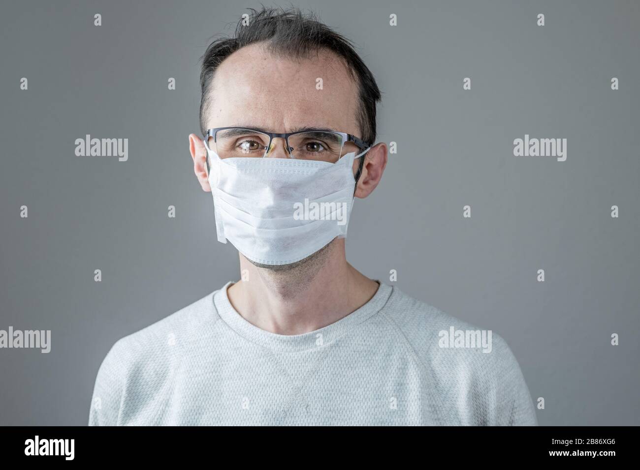 Adult man wearing hygienic mask to prevent infection, airborne respiratory illness such as flu, 2019-nCoV on gray background. Healthcare concept. Stock Photo