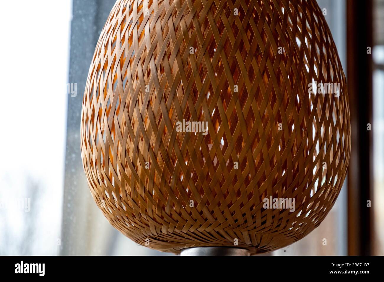 Wicker straw lampshade closeup. Natural crossed straw woven lattice texture with backlighting. Shaped lattice lamp. Light beige grid pattern. Geometri Stock Photo